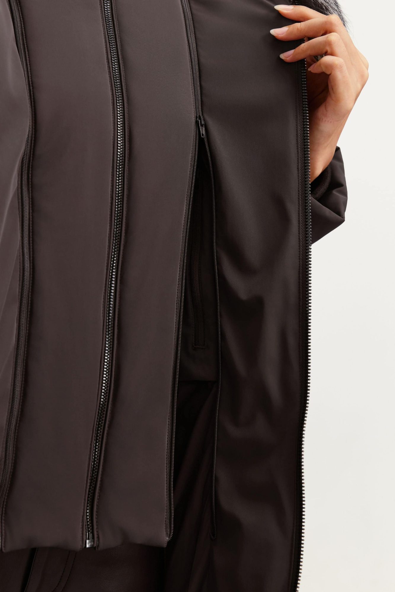 Close-up of dark brown puffer jacket showing vertical quilted seams and full-length front zipper with hand in pocket
