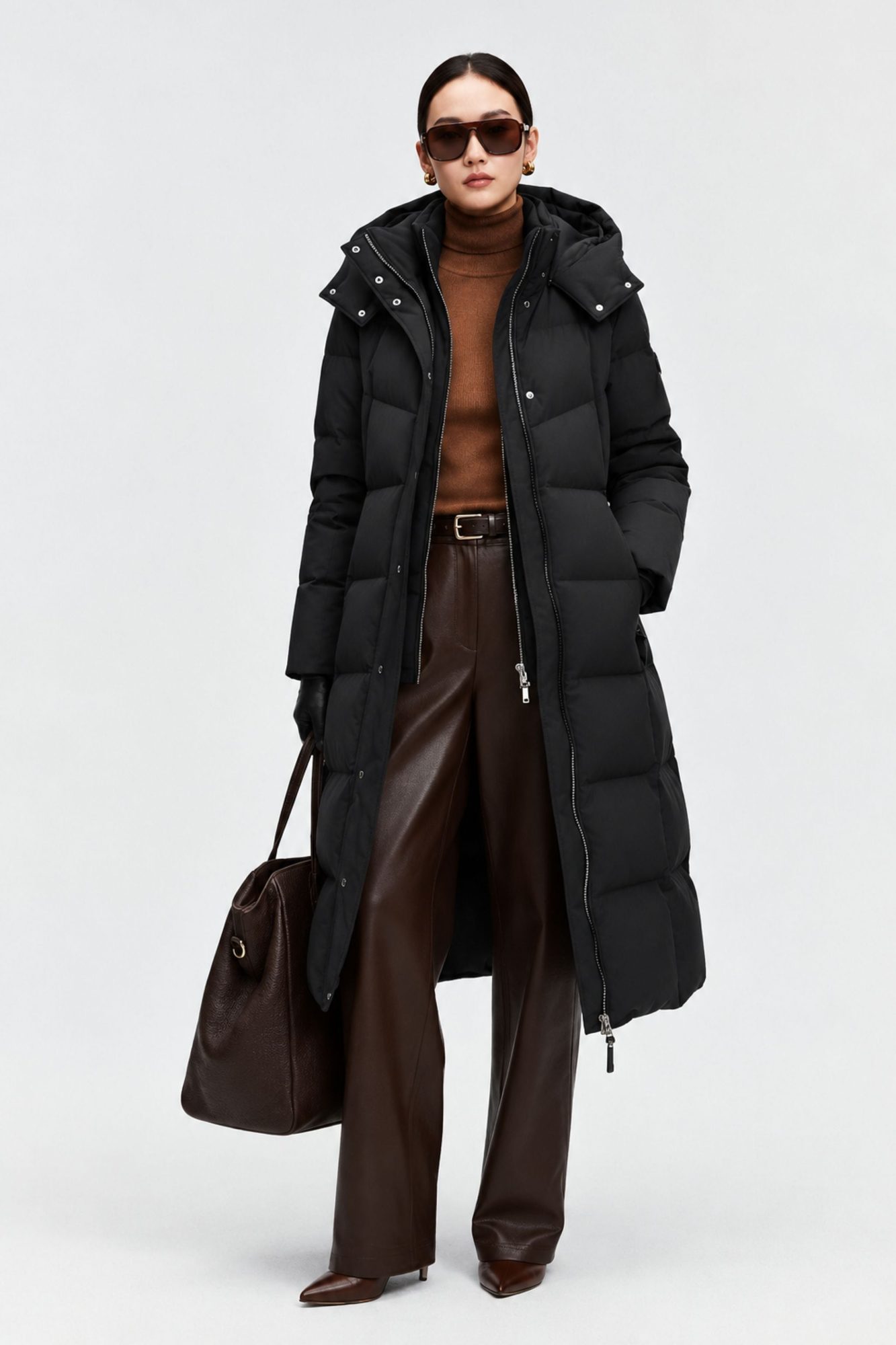 Woman wearing black puffer coat with brown sweater, brown leather pants, and carrying brown handbag